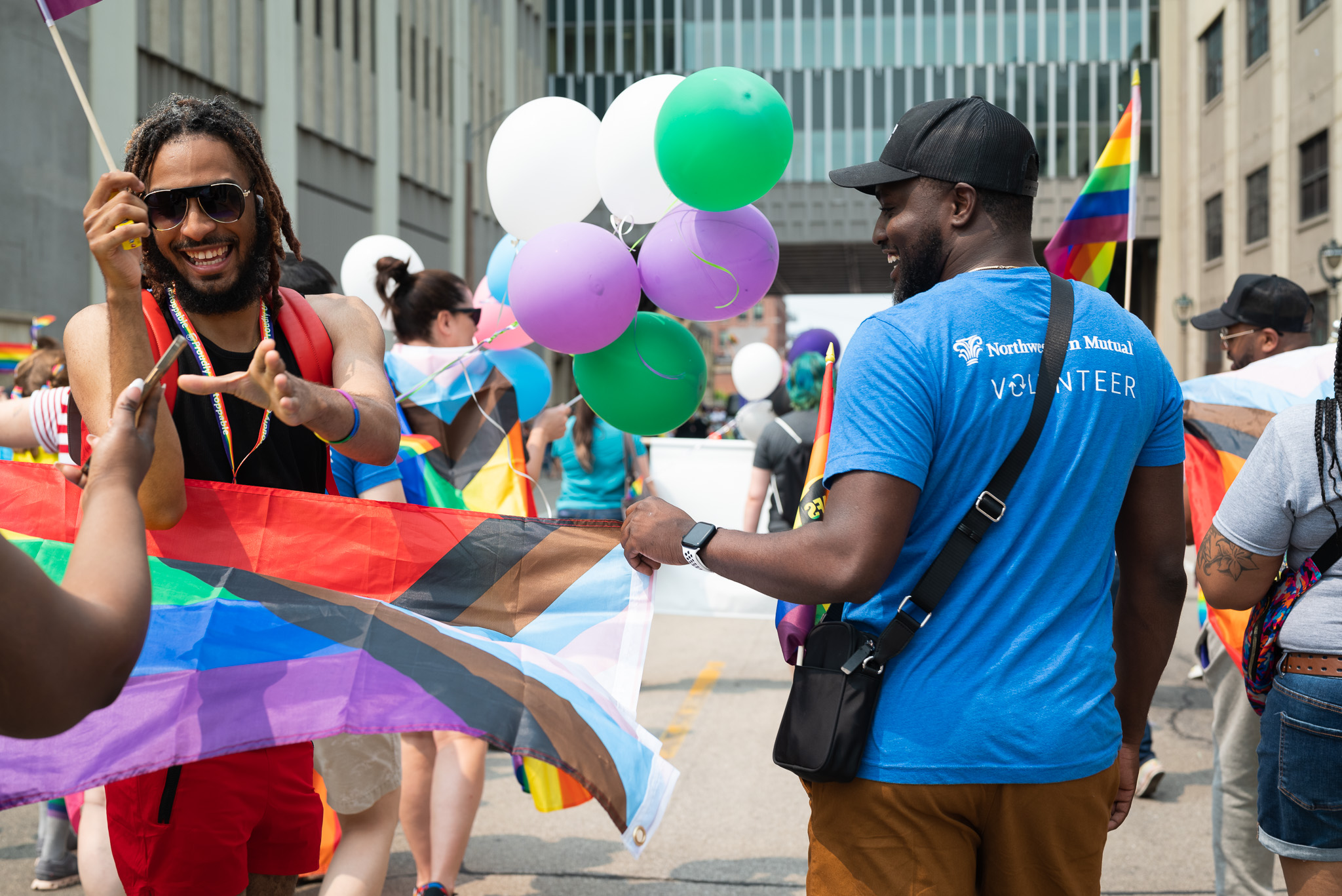 People holding rainbow flags and balloons in a parade, celebrating diversity and inclusion.